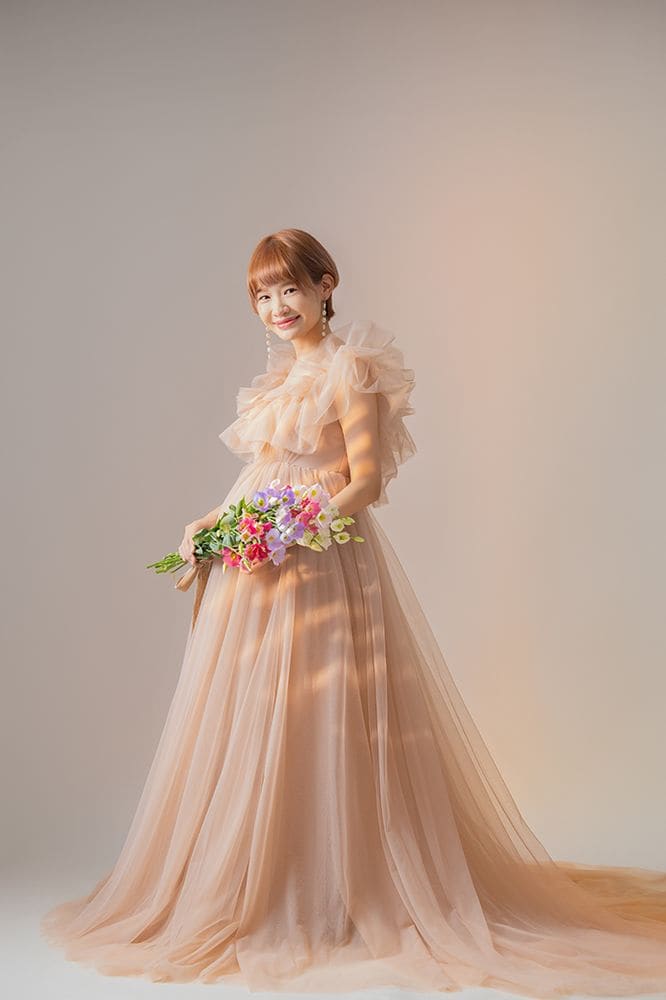 ピンクベージュのチュールドレス、花束を手に