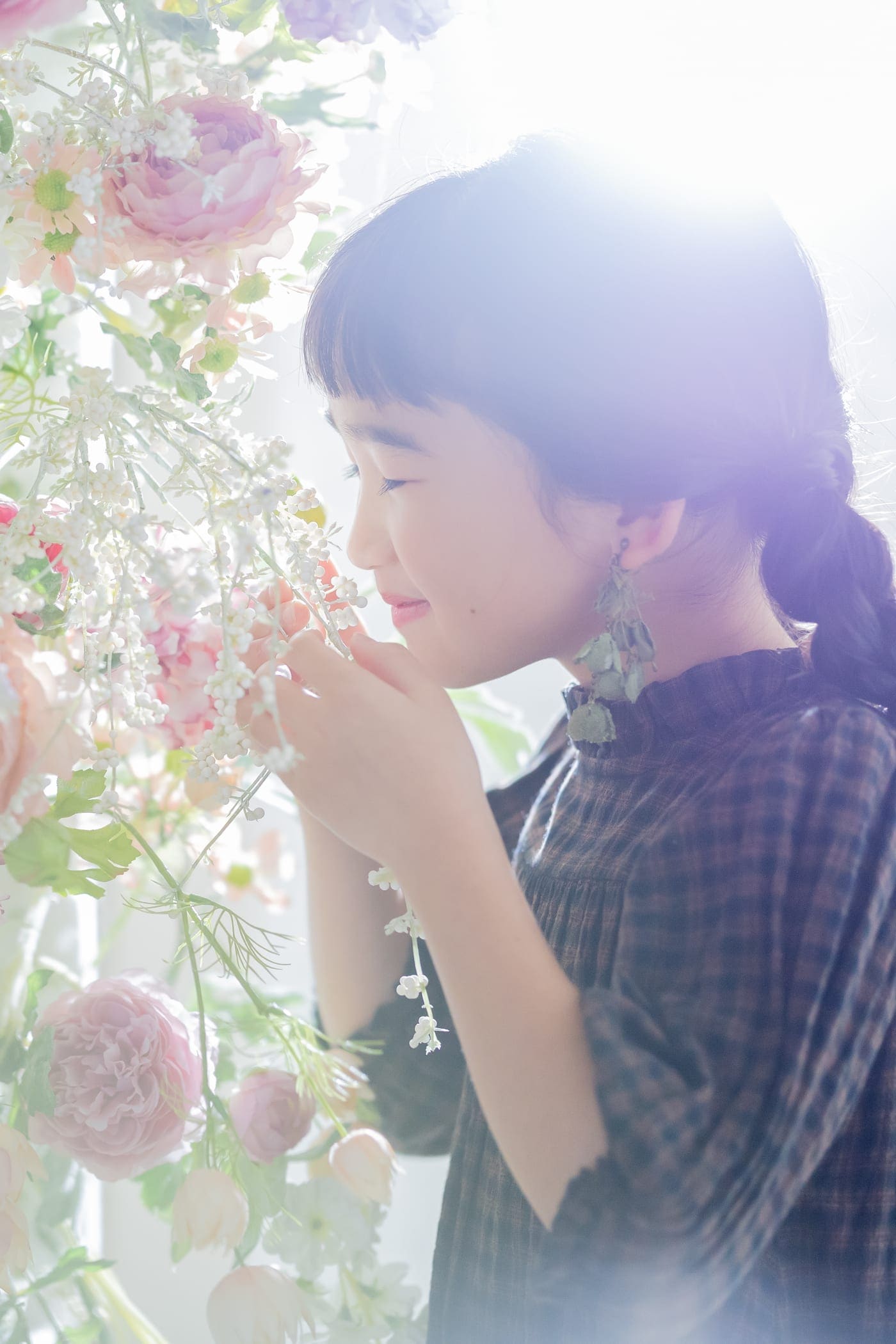 淡いピンクの花が咲き垂れるそばで、花の香りをかぐ女の子