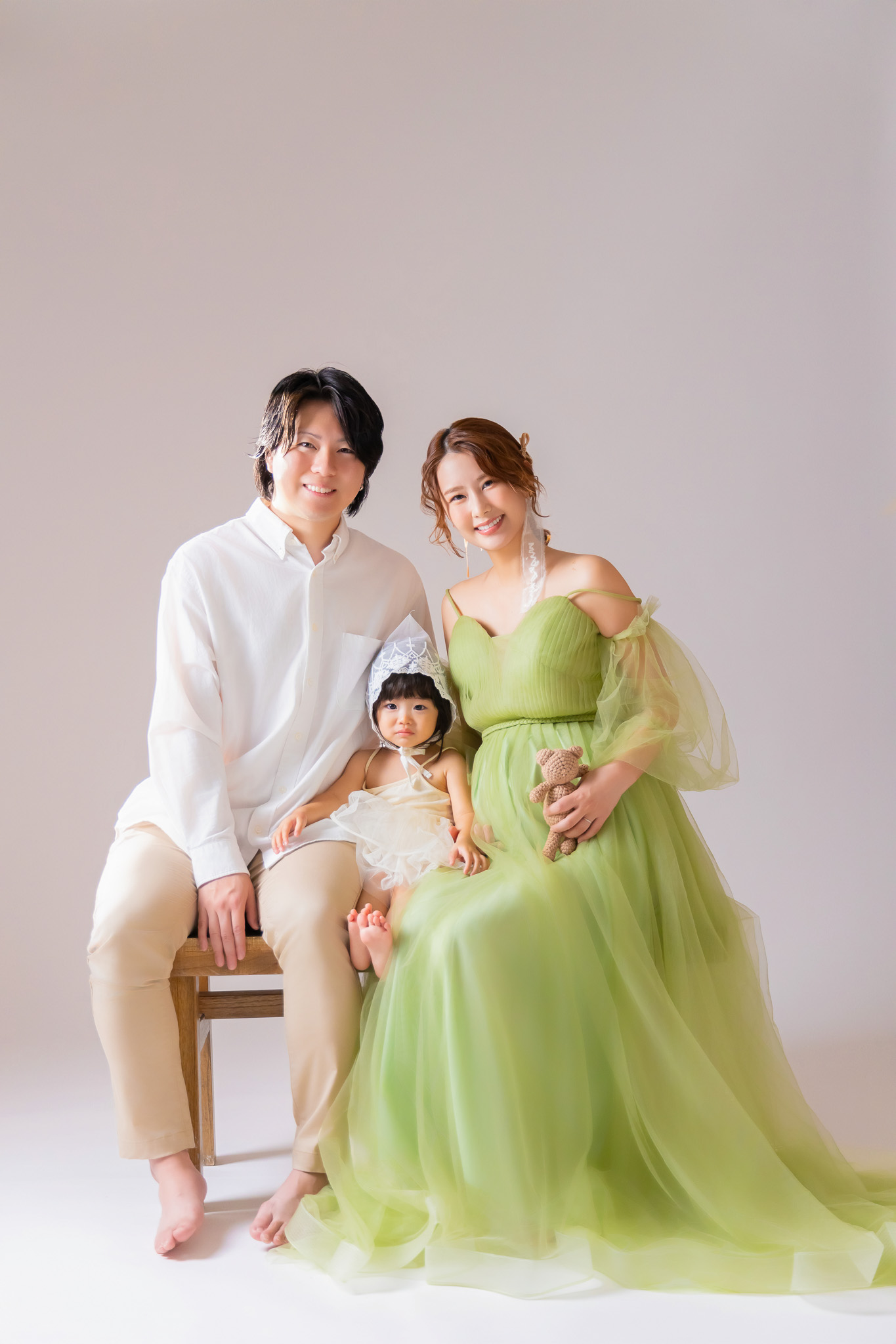 白いシャツとベージュのパンツの夫、グリーンのドレスの妊婦、白い衣装の女の子が並んで座る