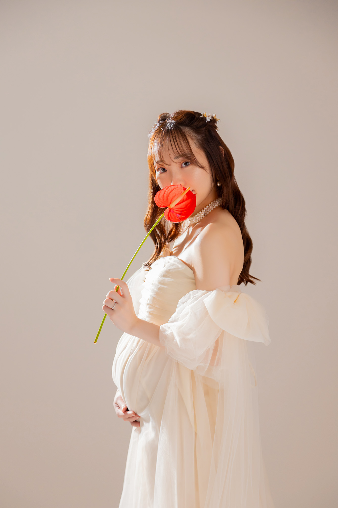 クリーム色のマタニティドレスをまとい、一輪の花を手にして微笑む姿