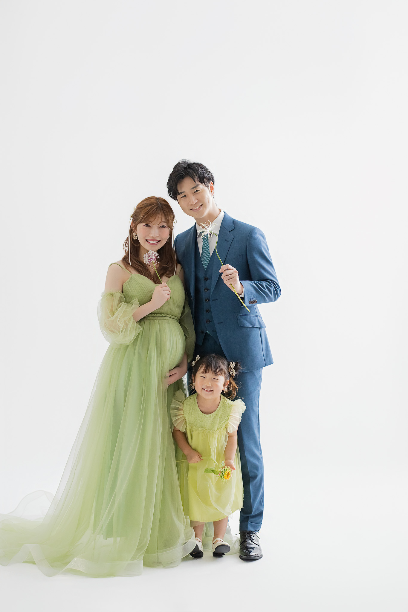 色のトーンを揃えた衣装で並ぶ、ご夫婦と上の子の家族写真