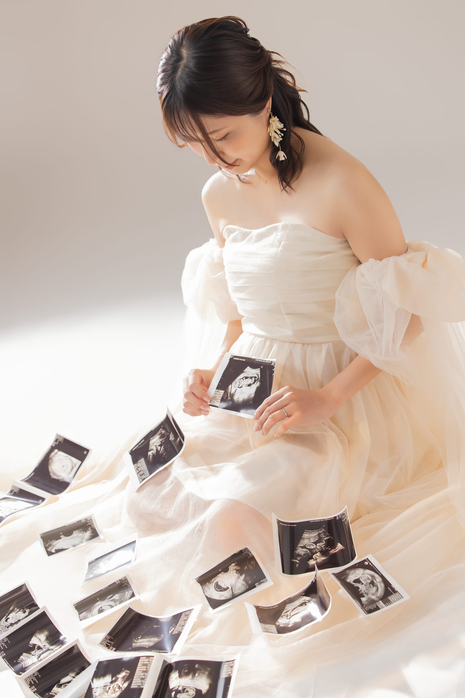 クリーム色のドレスで座り、エコー写真を並べる妊婦