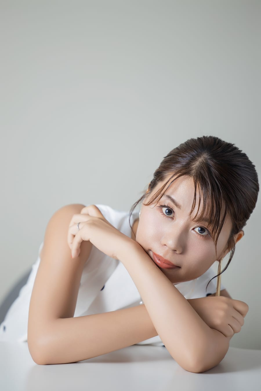 白い背景で頬杖をつき、正面を向いた明るい印象のプロフィール写真