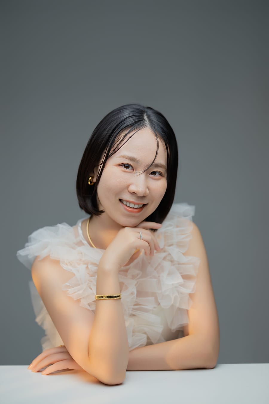 白いフリルのトップスで頬杖をつき、笑顔を見せたプロフィール写真