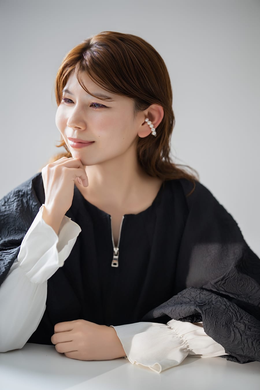 白と黒を合わせた装いで頬に手を添えた、笑顔のプロフィール写真